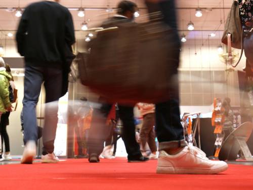 Blick aus der Froschperspektive auf die Schuhe von Menschen, die über einen roten Teppich gehen und eine Messe besuchen.