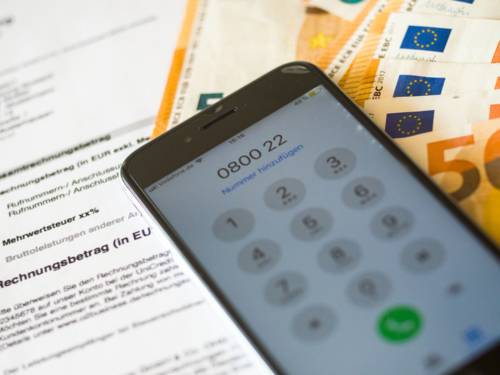 Ein Smartphone liegt auf Rechnungen und Fünfzigeuroscheinen, das Display zeigt die Wahl einer 0800-Rufnummer an.
