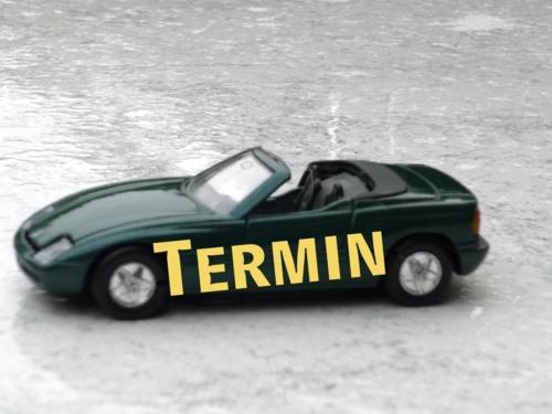 Grüner Wagen mit Seitenbeschriftung "Termin" auf regennaßem Untergrund