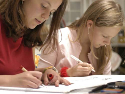Zwei Schülerinnen an einem Tisch, die konzentriert an Aufgaben auf Arbeitsblättern arbeiten.