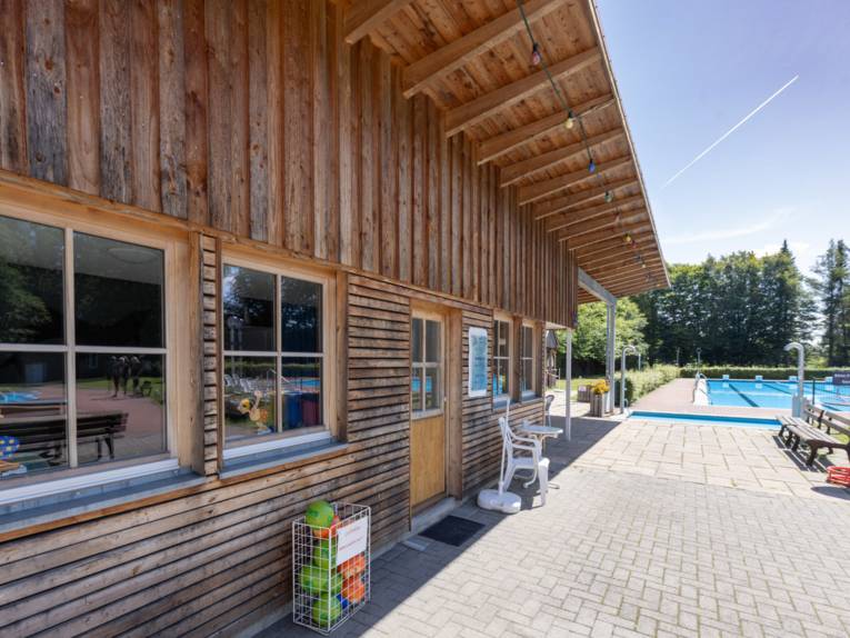 Freibad: Holzverkleidetes Gebäude, im Hintergrund Schwimmbecken