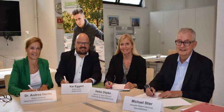 Zwei Männer und zwei Frauen sitzen an Konferenztischen und unterschreiben Dokumente. Vor Ihnen sind Namensschilder.