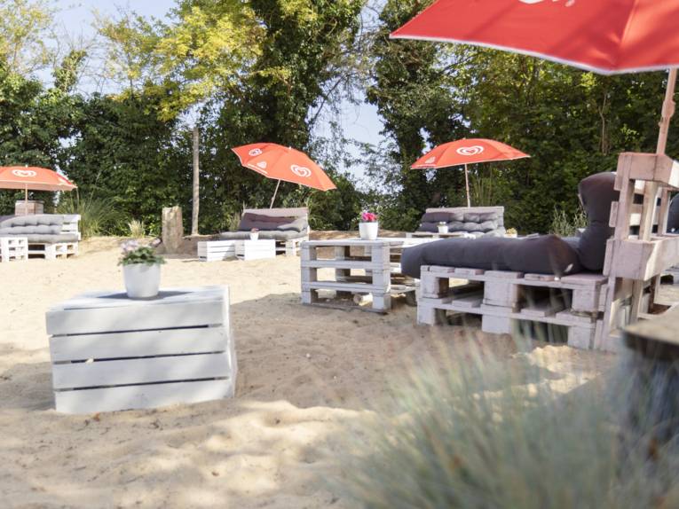 Große Sandfläche mit Sitzgelegenheiten aus Palletten mit Kissen, Pallettentische mit Blumen
