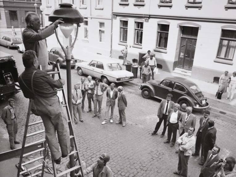 Arbeiter auf einer Leiter an einer Straßenlaternen. Historische Schwarz-Weiß-Aufnahme