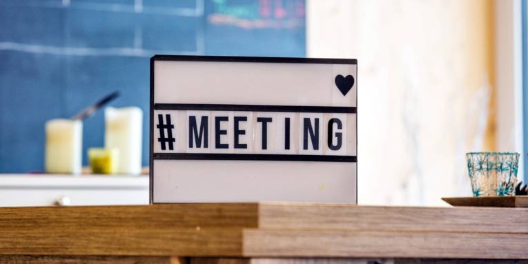 Auf einem Tisch steht ein beleuchtbares Schild mit den Zeichen: "#MEETING".