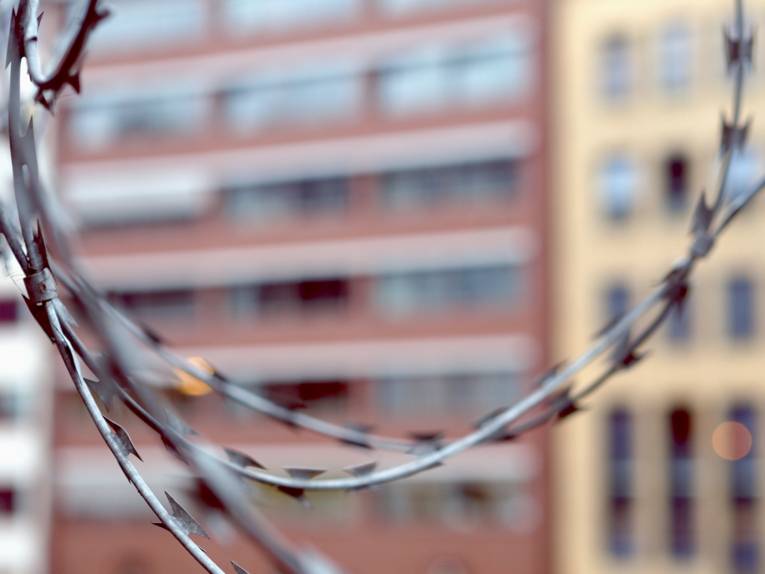 Vor einer unscharfen Häuserkulisse ringelt sich klingenbewährter Stacheldraht.