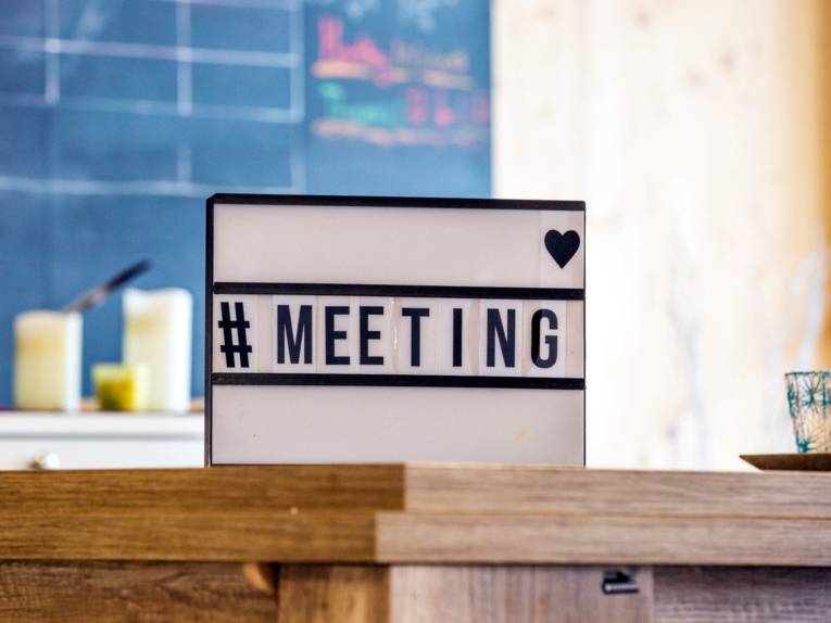 Auf einem Tisch steht ein beleuchtbares Schild mit den Zeichen: "#MEETING".