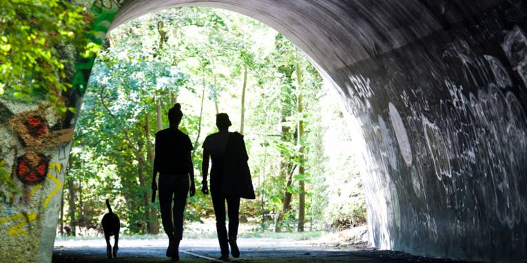 Zwei Menschen und ein Hund gehen durch einen Tunnel.