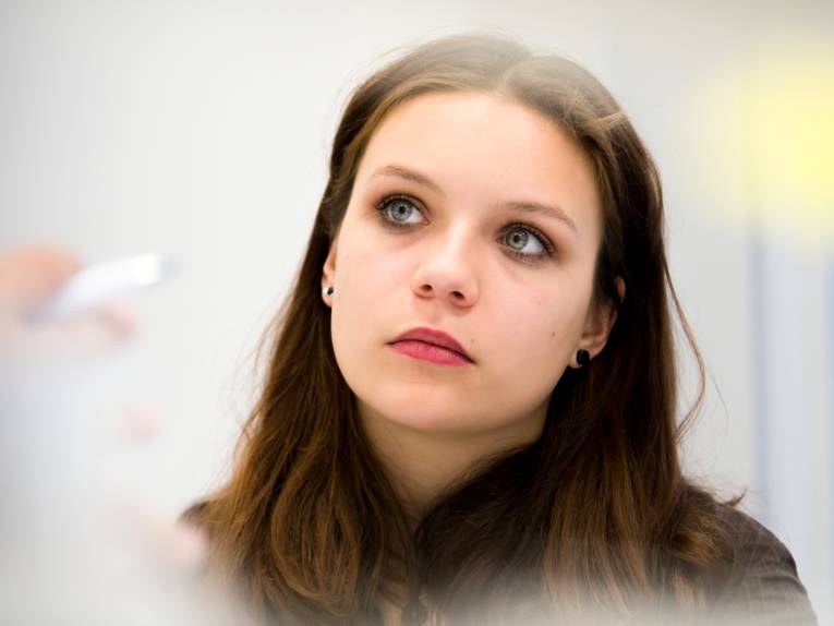 Eine junge Frau schaut gedankenverloren in die Kamera.