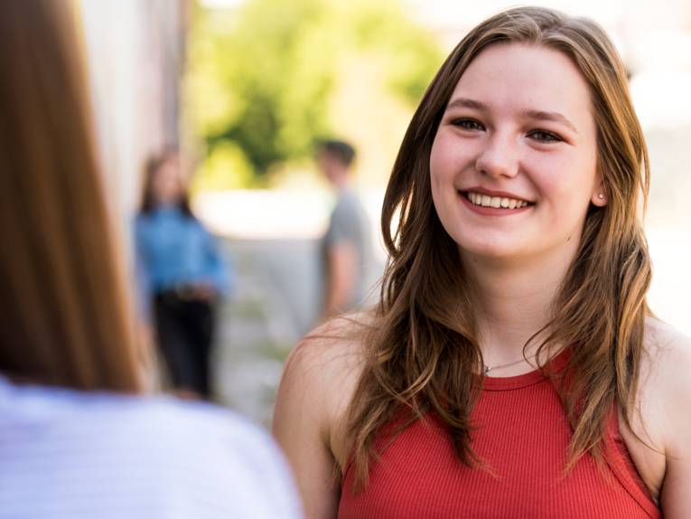 Zwei Frauen stehen sich gegenüber, im Hintergrund sind weitere Personen verschwommen zu erkennen.