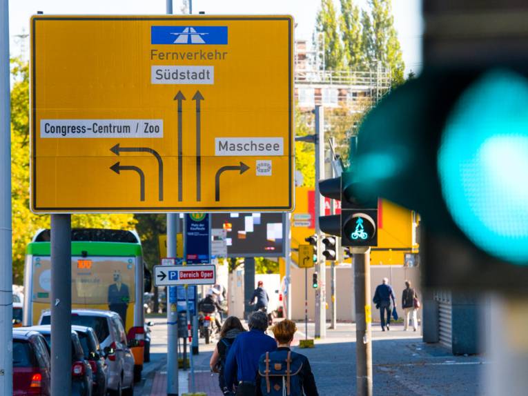 Ampeln für Autoverkehr, Fußgänger und Radfahrende stehen auf Grün, ein Wegweiser weist dem Verkehr den Weg in verschiedene Richtungen.