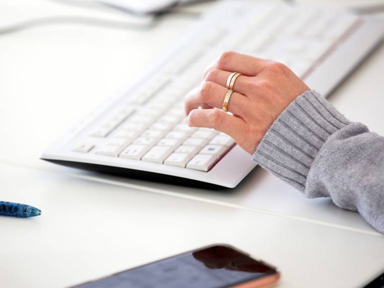 Eine Hand ist über einer Computertastatur, ein Smartphone liegt daneben.