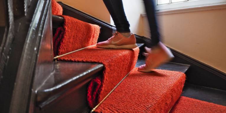 Jemand geht eine Treppe hinauf, auf den Stufen liegt roter Teppich.