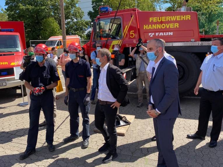 Mehrere Personen mit Masken vor Feuerwehr-Fahrzeugen. 