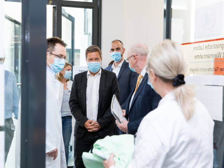 Mehrere Personen mit Schutzmasken in einer Forschungseinrichtung, darunter Oberbürgermeister Belit Onay und Politiker Robert Habeck.