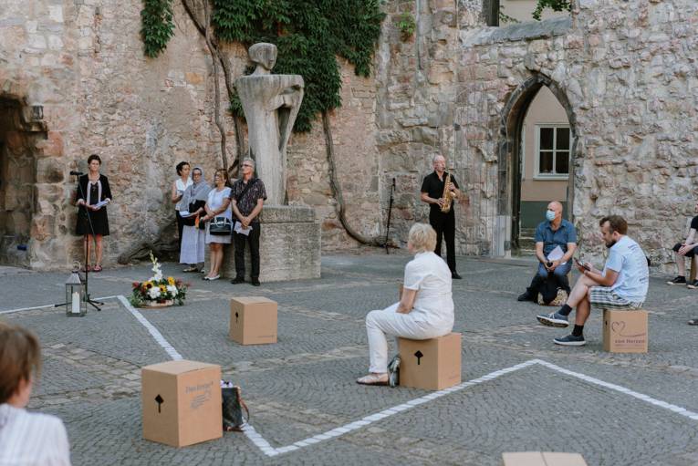Mehrere Menschen sitzen auf Pappkartons verteilt in der Aegidienkirche, im Hintergrund ein Saxophonspieler.