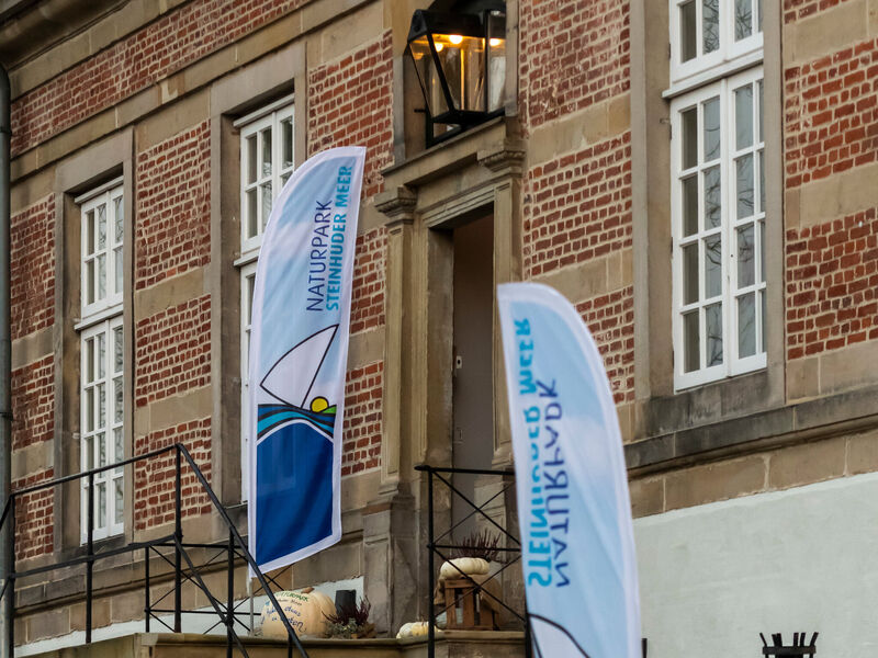 Zwei Beachflags mit dem Logo des Naturparks Steinhuder stehen auf einer Treppe zu einem Eingang von Schloss Landestrost in Neustadt am Rübenberge. Zwei Beachflags mit dem Logo des Naturparks Steinhuder stehen auf einer Treppe zu einem Eingang von Schloss Landestrost in Neustadt am Rübenberge.
